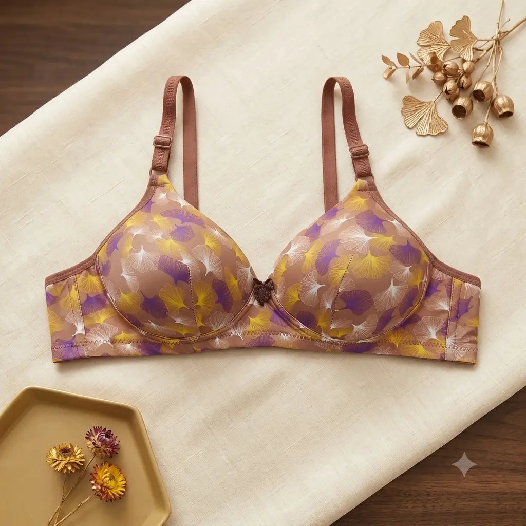 A wireless underwire bra with a brown and purple abstract floral pattern, laid flat on a cream-colored fabric background with decorative dried flowers.