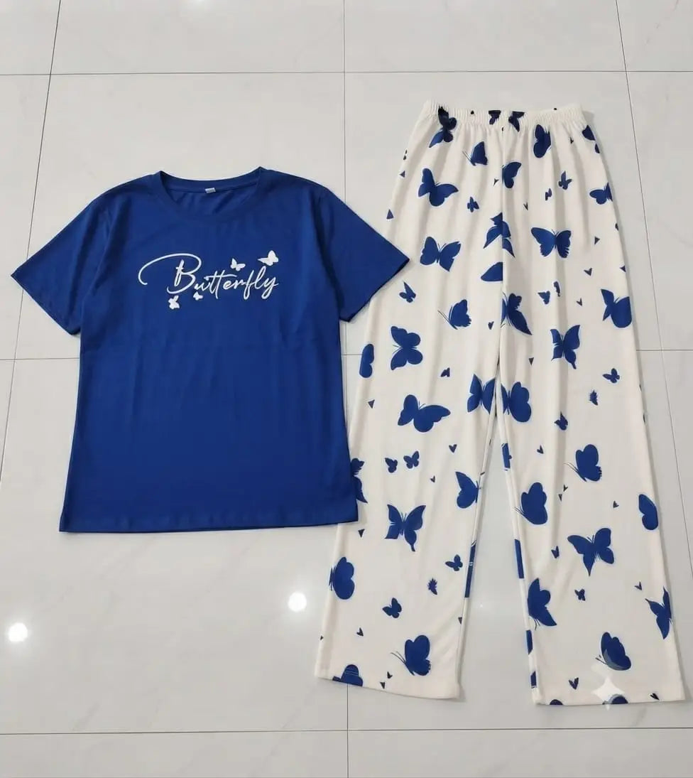 A two-piece pajama set laid flat on a light gray tiled floor, featuring a royal blue short-sleeve t-shirt with 'Butterfly' printed in white script, and white pants with a blue butterfly pattern.