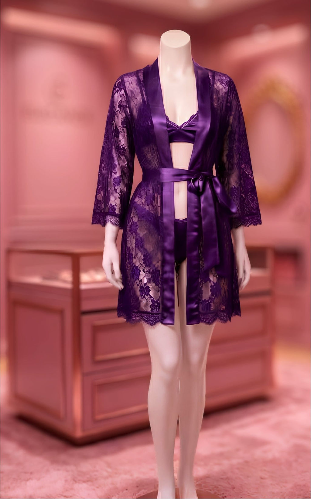 A purple lace robe with matching satin lingerie displayed on a mannequin in a softly lit pink boutique interior.