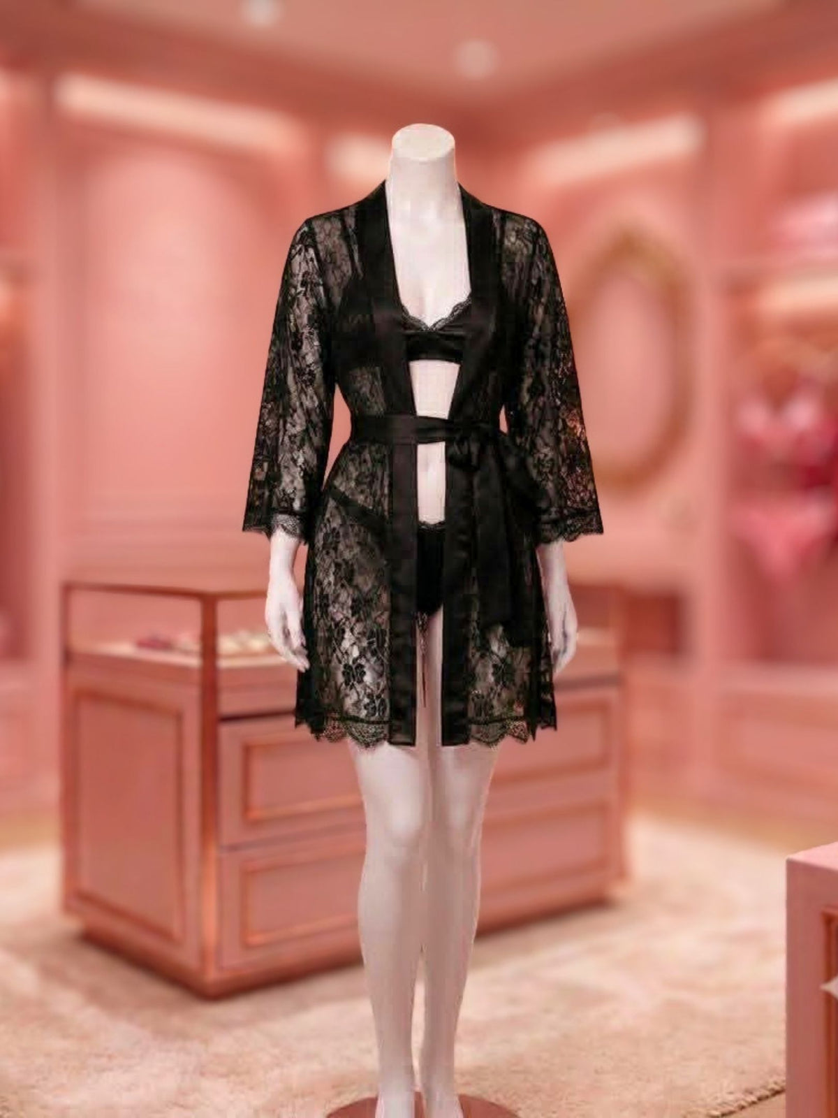 A mannequin wearing a black lace robe over a matching black lingerie set, displayed in a softly lit pink boutique interior.