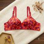 Red floral print underwire bra with adjustable shoulder straps, laid flat on a cream-colored fabric background with decorative dried flowers.