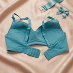 A teal long-sleeve underwire bra laid flat on a peach satin background, with matching teal strap and bow accessories placed nearby.
