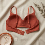 A terracotta-colored long-sleeve bralette with adjustable underwire cups and a matching band, laid flat on a textured beige fabric background with decorative props.
