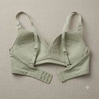 A sage green wireless bra with long sleeves and adjustable straps, laid flat on a textured beige fabric background.