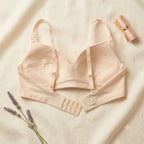 A light beige seamless bra laid flat on a cream-colored fabric background, styled with lavender sprigs and a matching rolled fabric accessory.