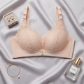 A light peach-beige wireless bra with lace cups and adjustable straps, styled in a flat-lay on a draped satin fabric with jewelry and a perfume bottle nearby.