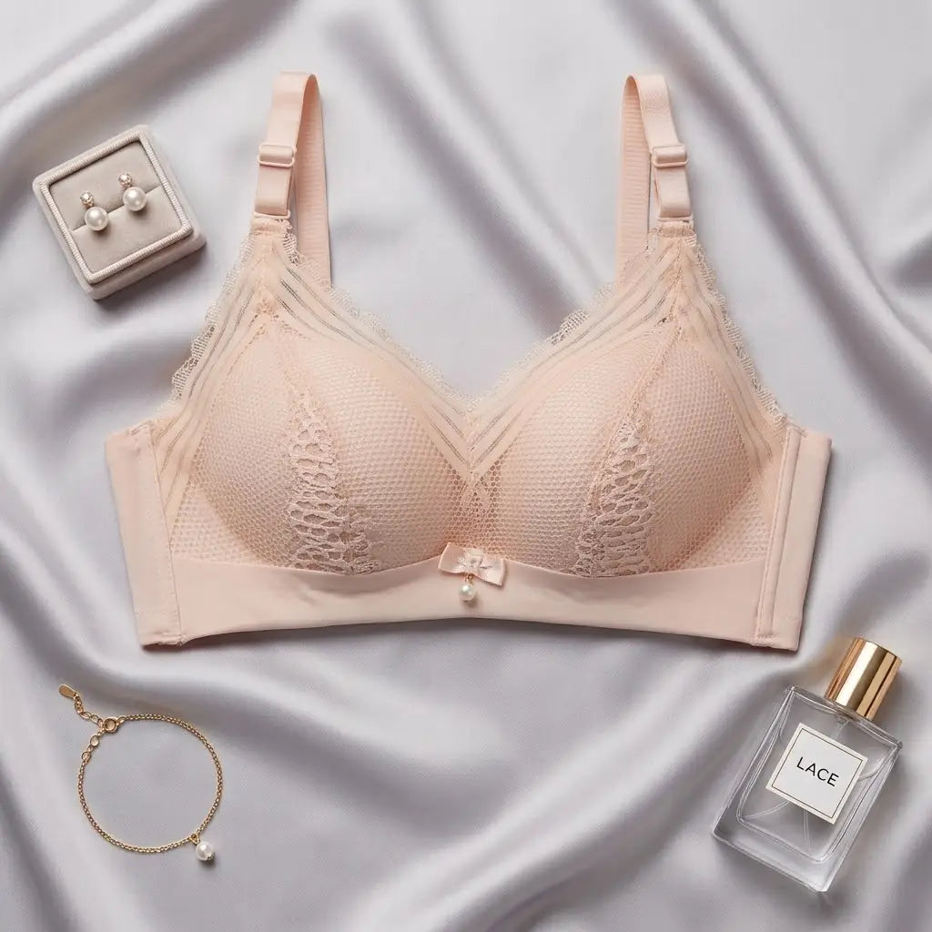 A light peach-beige wireless bra with lace cups and adjustable straps, styled in a flat-lay on a draped satin fabric with jewelry and a perfume bottle nearby.