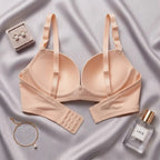A light peach-beige wireless underwire bra with adjustable straps and a rear hook-and-eye closure, presented in a flat-lay arrangement on a draped satin fabric background alongside jewelry and a perfume bottle.