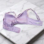 A lavender purple seamless bra with lace trim and an adjustable hook-and-eye back strap, displayed on a white marble background. The brand name 'AURA PARIS' is visible on a small label on the side.