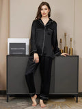 Woman wearing black satin pajamas standing next to a cabinet with decorative items.
