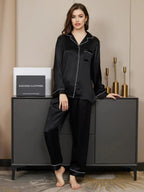 Woman wearing black satin pajamas standing next to a cabinet with decorative items.
