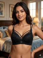A woman modeling a black lace bra in a softly lit bedroom setting. The bra features thin adjustable straps, delicate lace cups, and a small bow detail at the center front.
