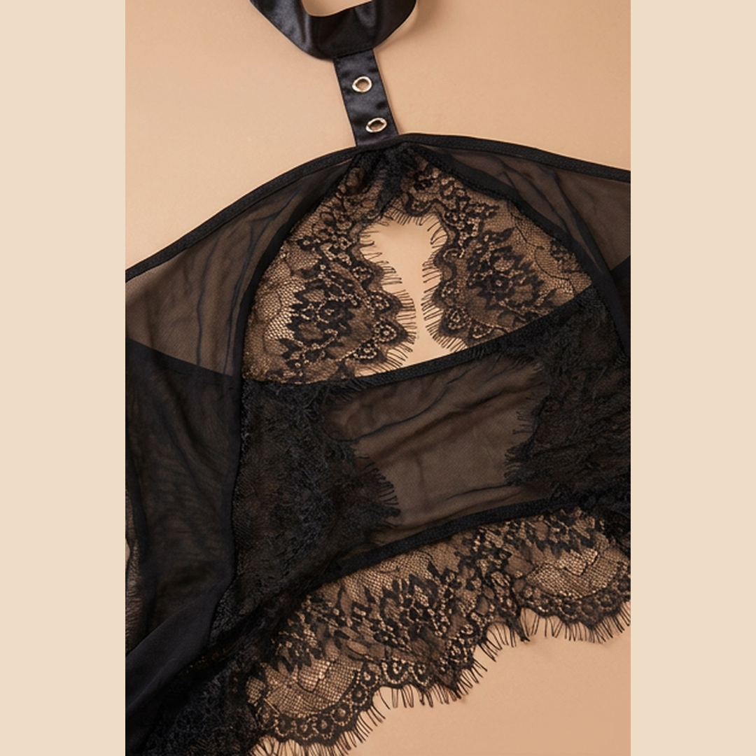 Black sheer mesh and lace lingerie top with a halter-style strap and decorative lace trim, shown against a warm beige background.