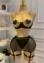Black sheer mesh lingerie set with gold chain straps and rhinestone heart details on a beige mannequin torso, photographed indoors against a white paneled wall.